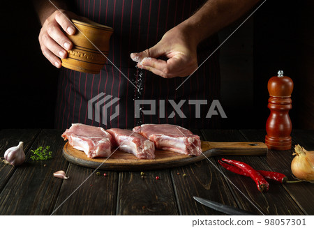 The cook salts raw sliced meat steaks on the cutting board of the kitchen before preparing dinner. Delicious grill idea 98057301