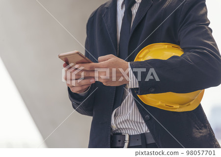 Construction engineer holding yellow hard hat holding smartphone. Safety helmet Holding Yellow hardhat using smartphone to communicate on Construction Site. Hardhat Protect Civil Construction concept 98057701