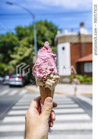 Ice cream in hand. Waffle cone with ice cream on the background of the street in the summer on a hot day. Street food, sweets, desserts concept. Ice cream in hand. Waffle cone with ice cream on the background of the street in the summer on a hot day. Street food, sweets, desserts concept. 98057818
