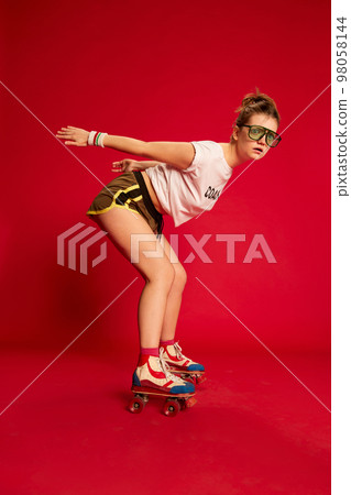 Scared fashionable stylish young girl in t-shirt and shorts rollerblading over red background. Youth, fashion, happy emotions and active lifestyle concept Scared fashionable stylish young girl in t-shirt and shorts rollerblading over red background. Youth, fashion, happy emotions and active lifestyle concept 98058144
