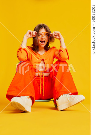 Excited girl in orange croptop and trousers with skateboard over colorful yellow background. Youth, fashion, actvie lifestyle, happy emotions and active lifestyle concept Excited girl in orange croptop and trousers with skateboard over colorful yellow background. Youth, fashion, actvie lifestyle, happy emotions and active lifestyle concept 98058202