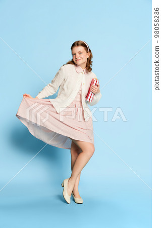 Dance. Portrait of funny beautiful girl in vintage style outfit posing over blue background. Retro fashion, business, education and emotions 98058286