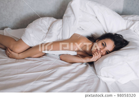 sexy nude brunette girl lying in bed under a blanket 98058320