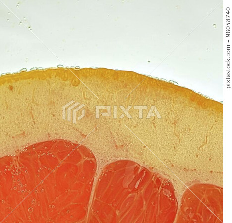 Close-up of a grapefruit slice in liquid with bubbles. Slice of red ripe grapefruit in water. Close-up of fresh grapefruit slice of red on white background 98058740