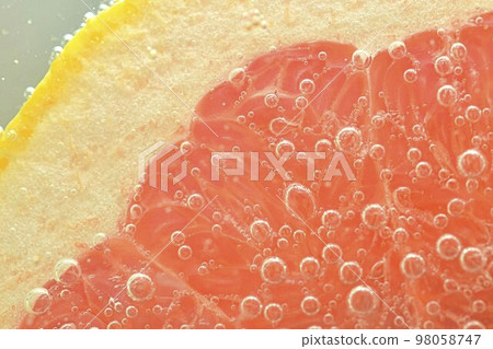 Close-up of fresh grapefruit slice on white background. Slice of red grapefruit in sparkling water on white background, close-up. Horizontal image 98058747