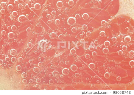 Close-up of a grapefruit slice in liquid with bubbles. Slice of red ripe grapefruit in water. Close-up of fresh grapefruit slice covered by bubbles 98058748