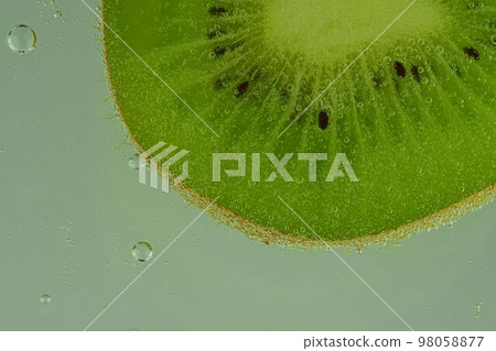 Close-up of kiwi fruit in liquid with bubbles. Slice of green ripe kiwi fruit in sparkling water. Juicy kiwi fruit in carbonated water. Macro image Close-up of kiwi fruit in liquid with bubbles. Slice of green ripe kiwi fruit in sparkling water. Juicy kiwi fruit in carbonated water. Macro image 98058877