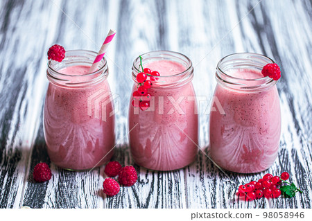 Side view of three jars with yogurt smoothie with cranberry, raspberry on wood table. Fruit dessert Side view of three jars with yogurt smoothie with cranberry, raspberry on wood table. Fruit dessert 98058946