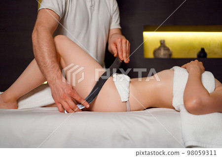 Male physiotherapist performing scraping massage on legs muscle of woman on clinic 98059311