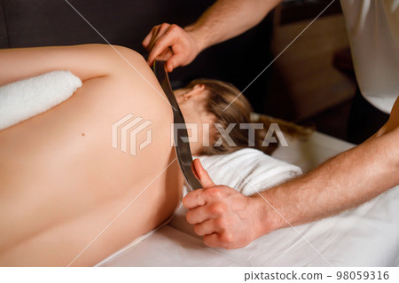 Woman receives a special medical back massage using a special stainless steel tool 98059316