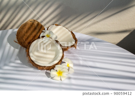 Tropical fruit concept, Halves of fresh coconut and plumeria flower with leaves shadow Tropical fruit concept, Halves of fresh coconut and plumeria flower with leaves shadow 98059412