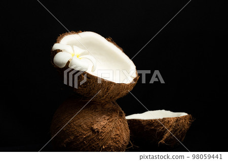 Tropical fruit concept, Halves of fresh white coconut and plumeria flower on black background 98059441