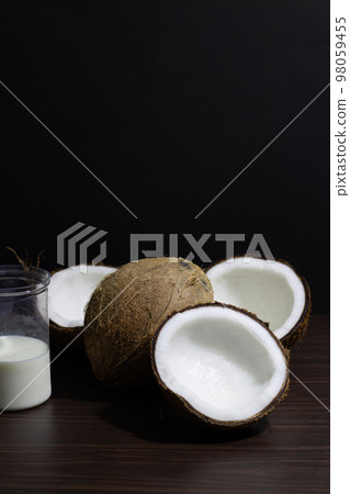 Tropical fruit concept, Halves of fresh coconuts and glass of coconut milk on wooden background 98059455