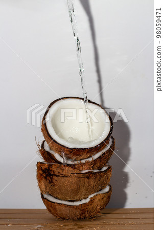 Tropical fruit concept, Coconut water pouring into fresh coconut halves stacked on wood background Tropical fruit concept, Coconut water pouring into fresh coconut halves stacked on wood background 98059471