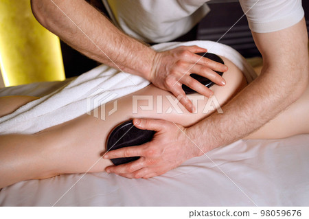 Male masseur doing lastone therapy. Close-up of a woman enjoying buttocks massage with warm stones Male masseur doing lastone therapy. Close-up of a woman enjoying buttocks massage with warm stones 98059676