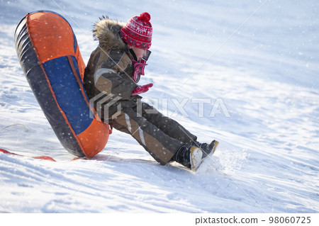 A happy boy up in the air on a tube sledding in the snow.. A boy slides down a hill in winter. A happy boy up in the air on a tube sledding in the snow.. A boy slides down a hill in winter. 98060725