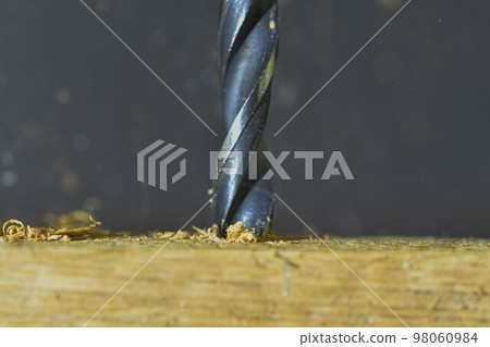 Rotating drill in wood. Drill with flying wood chips. Concept for carpentry, crafts, DIY. Macro and close-up image Rotating drill in wood. Drill with flying wood chips. Concept for carpentry, crafts, DIY. Macro and close-up image 98060984