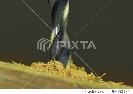 Rotating drill in wood. Drill with flying wood chips. Concept for carpentry, crafts, DIY. Macro and close-up image Rotating drill in wood. Drill with flying wood chips. Concept for carpentry, crafts, DIY. Macro and close-up image 98060985