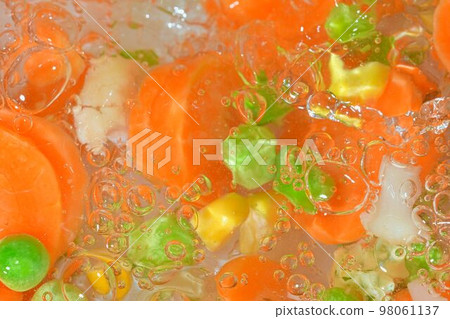 Close-up fresh soup vegetables with carrots, peas, cauliflower and corn on white background. Soup vegetables with carrots, peas, cauliflower and corn in boiling water on white background, close-up. Close-up fresh soup vegetables with carrots, peas, cauliflower and corn on white background. Soup vegetables with carrots, peas, cauliflower and corn in boiling water on white background, close-up. 98061137