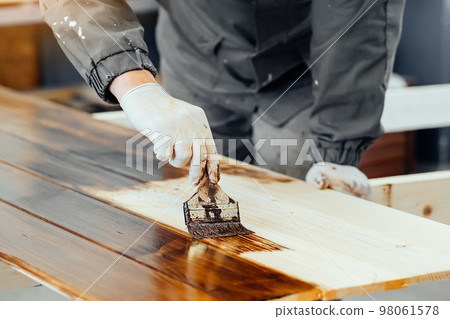 Man paints wooden boards with paint brush. Carpenter cabinetmaker varnishes wooden surface 98061578