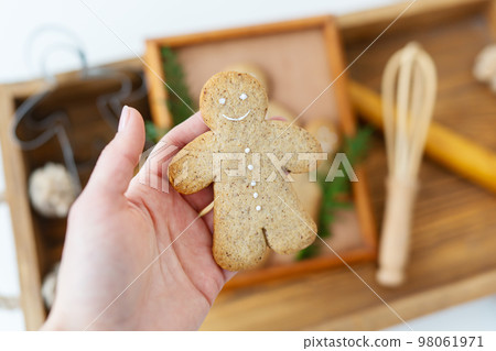 A woman's hand holds a gingerbread man. Cooking gingerbread at home lies on a wooden tray. Holiday concept. 98061971