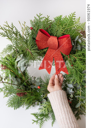 Stylish Christmas wreath for the interior, hang the wreath on the door. Handmade, the girl is holding a freshly made wreath with a beautiful red bow. Festive atmosphere. 98061974