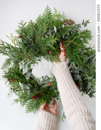 Stylish Christmas wreath for the interior, hang the wreath on the door. Handmade, the girl holds a freshly made wreath in her hands. The atmosphere of the holiday, Christmas and New Year. Stylish Christmas wreath for the interior, hang the wreath on the door. Handmade, the girl holds a freshly made wreath in her hands. The atmosphere of the holiday, Christmas and New Year. 98061975