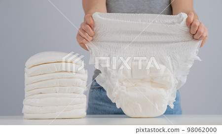 A woman chooses an adult diaper from a pile. Urinary incontinence problem. A woman chooses an adult diaper from a pile. Urinary incontinence problem. 98062000