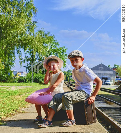 Adorable little girl and boy on a railway station, waiting for the train with vintage suitcases. Traveling, holiday and childhood concept. Travel insurance concept. Vacation trip. Adorable little girl and boy on a railway station, waiting for the train with vintage suitcases. Traveling, holiday and childhood concept. Travel insurance concept. Vacation trip. 98062016