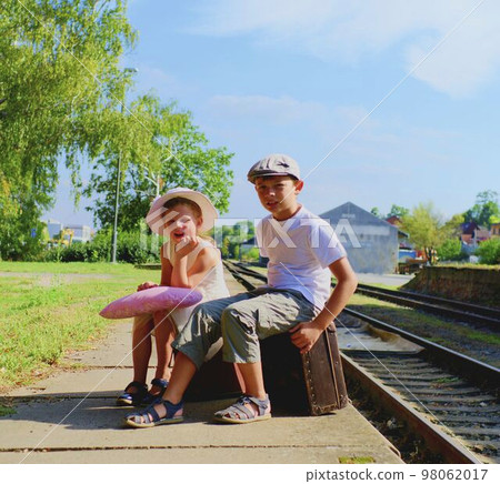 Adorable little girl and Adorable little girl and boy on a railboy on a railway station, waiting for the train with vintage suitcases. Traveling, holiday and childhood concept. Travel concept Adorable little girl and Adorable little girl and boy on a railboy on a railway station, waiting for the train with vintage suitcases. Traveling, holiday and childhood concept. Travel concept 98062017