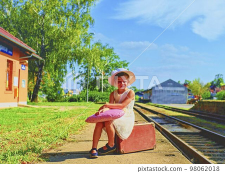 Adorable little girl on a railway station, waiting for the train with vintage suitcase. Traveling, holiday and childhood concept. Travel insurance concept. Adorable little girl on a railway station, waiting for the train with vintage suitcase. Traveling, holiday and childhood concept. Travel insurance concept. 98062018