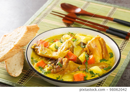 Coconut chicken curry with potatoes, onions and carrots served with a baguette close-up on a mat. Horizontal 98062042