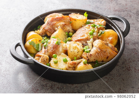 Chicken pieces with potato wedges and roasted in a lemon garlic white wine sauce close-up in a frying pan. Horizontal 98062052