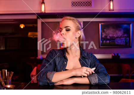 Young pretty woman smoke an electronic cigarette at the vape bar 98062611