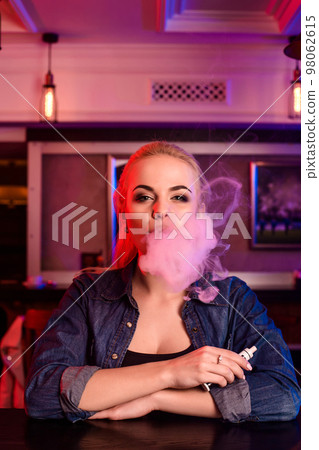 Young pretty woman smoke an electronic cigarette at the vape bar 98062615