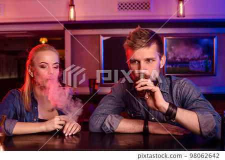 A man and woman smoking electronic cigarette in a vape bar. 98062642