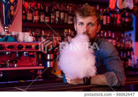 Vape. Vaping man in a cloud of vapor. Photo is taken in a vape bar. Vape. Vaping man in a cloud of vapor. Photo is taken in a vape bar. 98062647