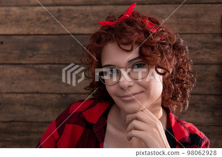 Portrait of a young smiling girl with curly hair against a background of boards. 98062928