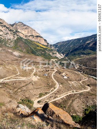 Mountain serpentine in sunlight. Dangerous narrow dirt mountain road through the hills to a high-altitude village. Vertical view. 98063187