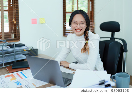 Portrait of a woman business owner showing a happy smiling face as he has successfully invested her business using computers and financial budget documents at work. 98063198
