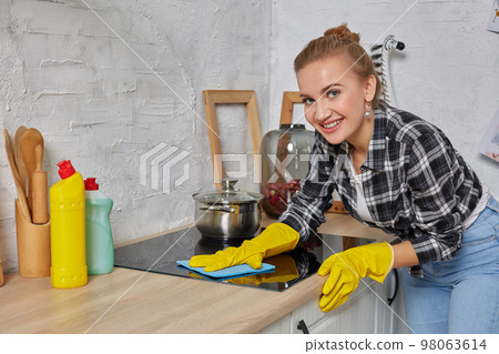 Blonde woman in protective gloves with rag cleaning electric stove at home kitchen. Girl washing black shiny surface of kitchen top Blonde woman in protective gloves with rag cleaning electric stove at home kitchen. Girl washing black shiny surface of kitchen top 98063614