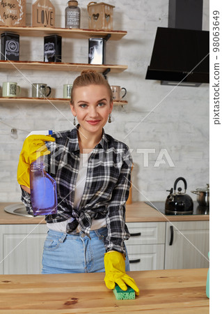 Beautiful woman in protective gloves cleaning kitchen table with rag and spray 98063649