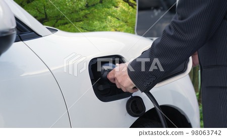 Progressive businessman charging EV car in the forest with charging station . 98063742
