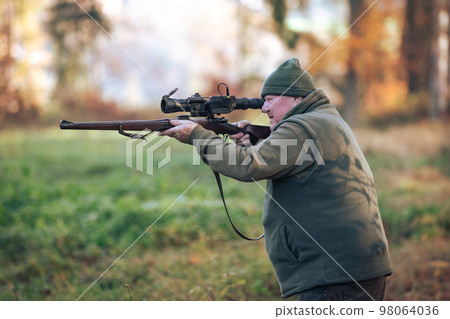Autumn hunting season, hunter with rifle looking out for some wild animal in a wood or forest, outdoor sports concept 98064036