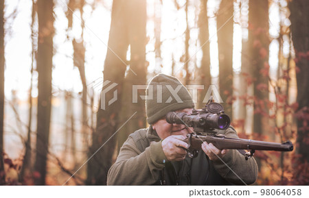 Autumn hunting season, hunter with rifle looking out for some wild animal in a wood or forest, outdoor sports concept Autumn hunting season, hunter with rifle looking out for some wild animal in a wood or forest, outdoor sports concept 98064058
