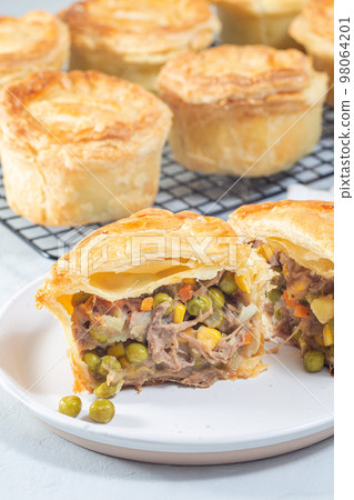 Sliced beef pot pie on plate, pies on cooling rack, vertical Sliced beef pot pie on plate, pies on cooling rack, vertical 98064201