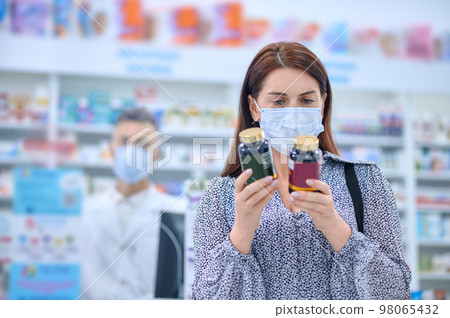 Woman in protective mask holding jars with vitamins in hands 98065432