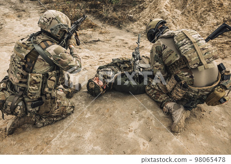 Wounded man lying on a ground, other soldiesr next to him 98065478