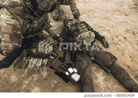 Soldiers near the wounded man examining him 98065484