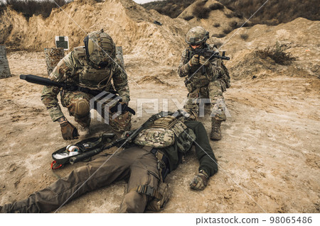 Soldiers near the wounded man examining him Soldiers near the wounded man examining him 98065486